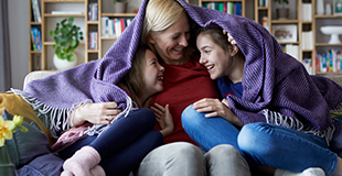 Mother under purple blanket with two children
