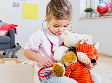 Young girl holding a stethoscope to her toys 375x279