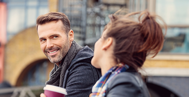 Man and women having a coffee outside on a bench.