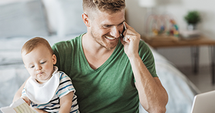 Young man speaking on his mobile, whilst holding his baby during breakfast